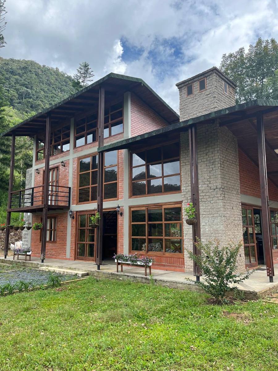 Two-storey mountain house in brick and timber, with the forest behind.
