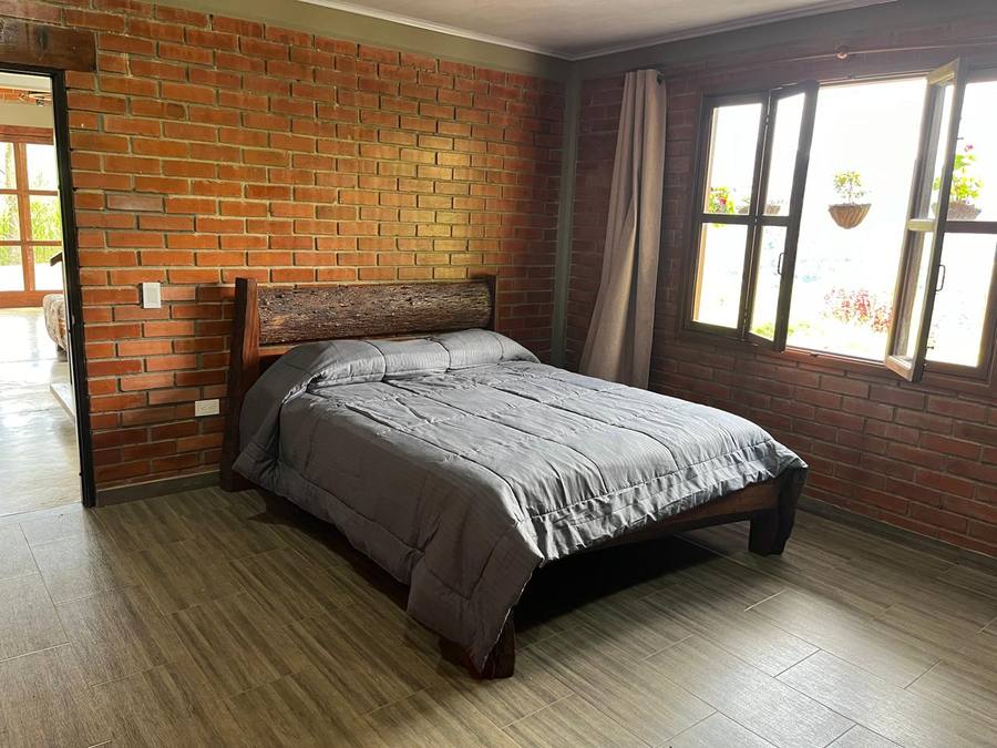 Room with an exposed brick wall and a headboard made from a raw timber beam.